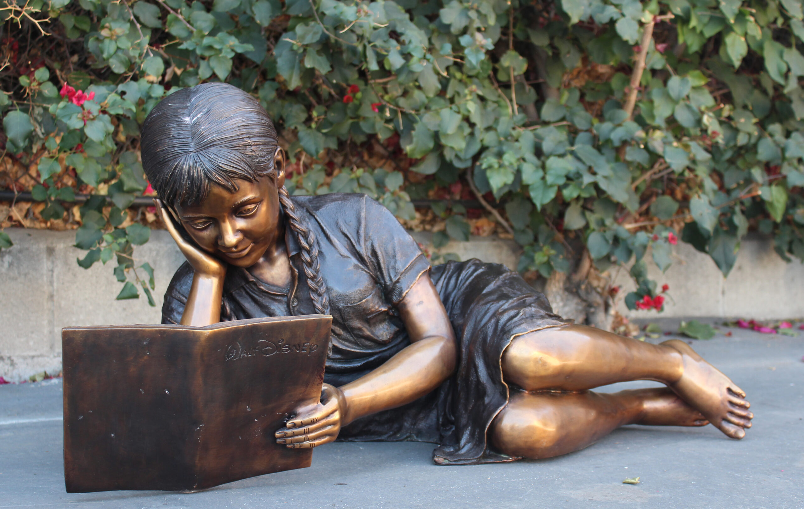 bronze statue of a girl laying down reading
