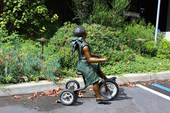 bronze statue of girl riding tricycle