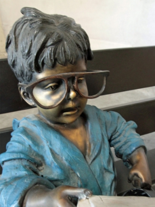 bronze statue of a boy on bench reading the newspaper