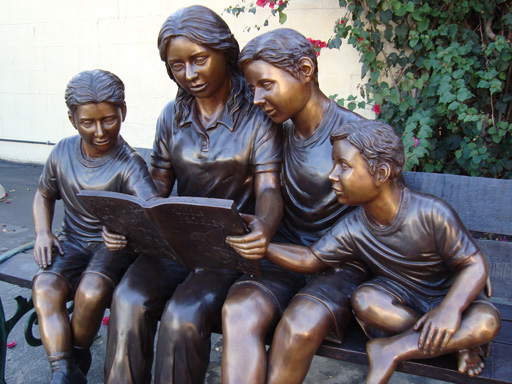 bronze statue of family reading on bench