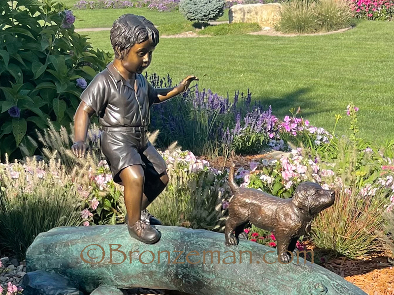 bronze statue of a boy and dog walking on a log