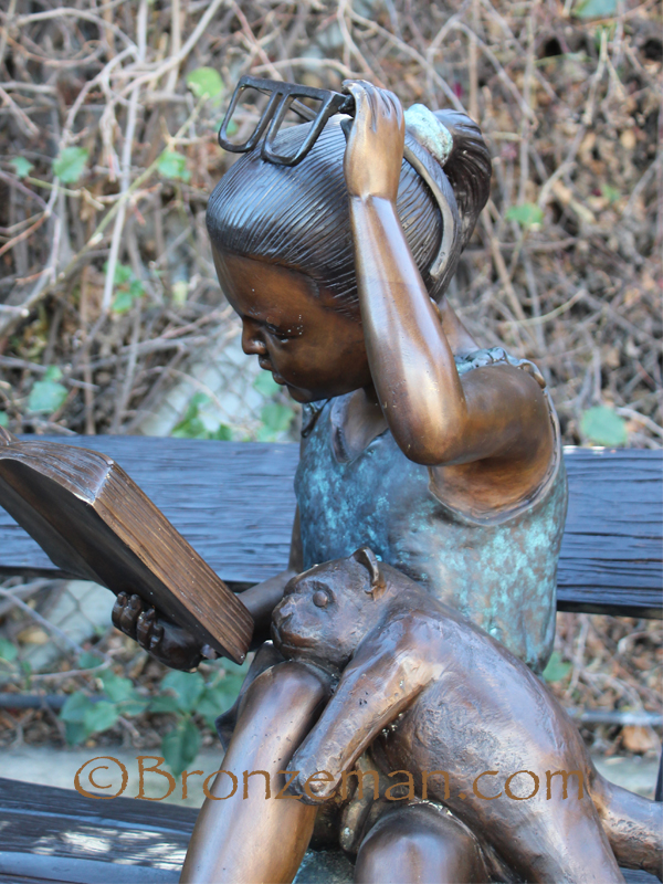 bronze statue of girl reading on bench