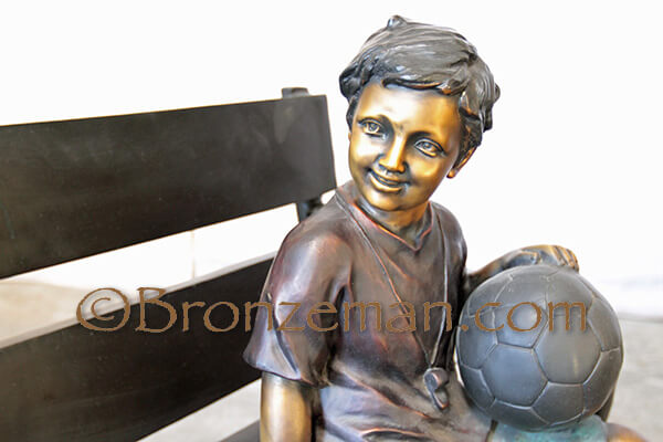 bronze statue of boy on bench with soccer ball