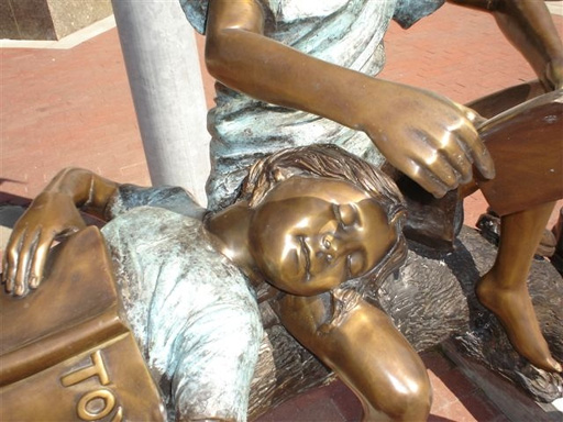 bronze statue of children reading on a log
