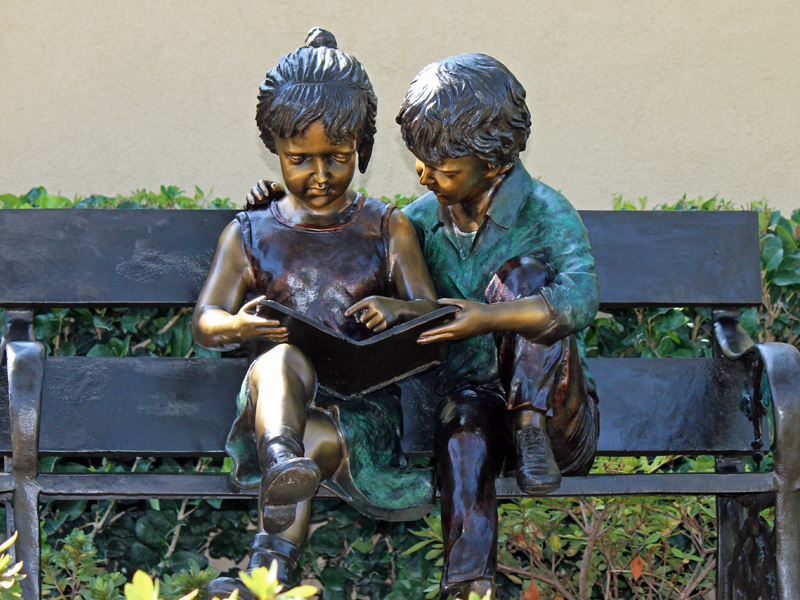 bronze statue of kids reading on bench